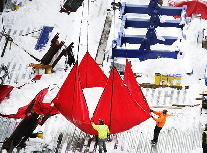 Workers guide a large, red tarp filled with snow as it is hoisted by a crane from the top deck of the Hudson Yards construction site, Monday, Jan. 25, 2016, in New York. Workers are clearing the construction site from the weekend snowstorm. (AP Photo/Mark Lennihan)